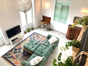 Uma sala de estar com um sofá verde, uma televisão, uma escrivaninha de madeira e um tapete estampado.