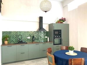 Cozinha com painel de azulejos em padrão herringbone, forno embutido e área de jantar com mesa e cadeiras.