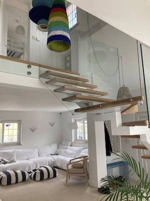 Ein modernes Interieur mit einer Glasstiege, weißen Möbeln und einem gestreiften Kissen.