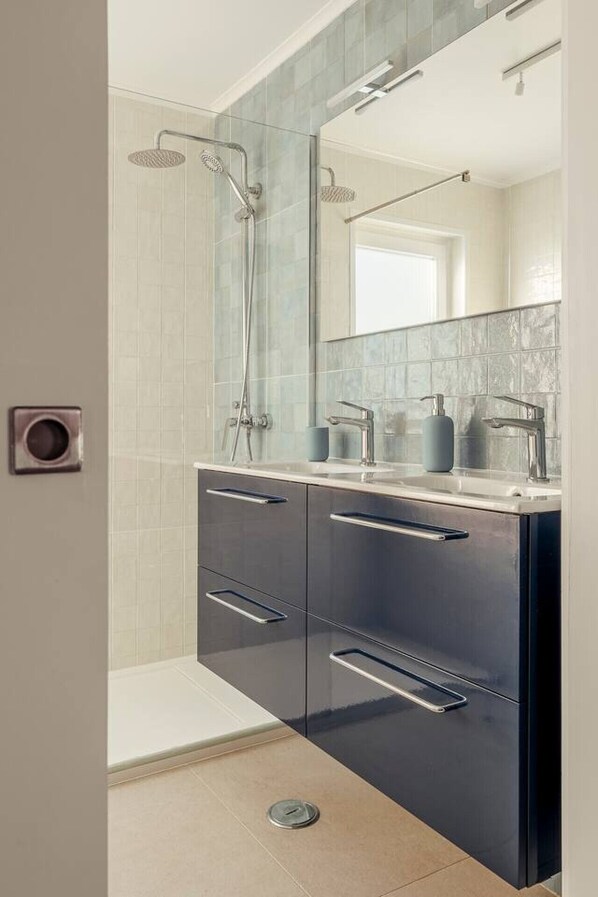 A modern bathroom with a glass shower enclosure, a large mirror, and a dual sink vanity.