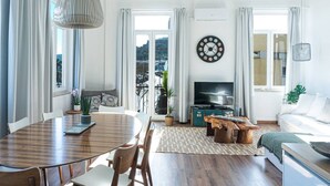 Ein modernes Wohnzimmer mit Essbereich, Fernseher und einem großen Fenster mit Vorhängen.