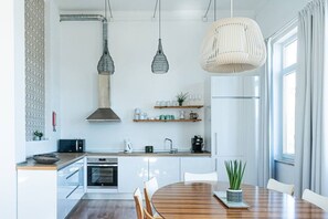 A modern kitchen with a central island, pendant lights, and a dining area with a round table. - Waterfront Living | Stunning Sea and Ocean Views (Setúbal)