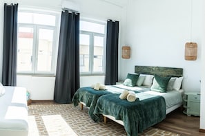 A bedroom with a bed, a nightstand, a window with curtains, and a view of buildings outside. - Waterfront Living | Stunning Sea and Ocean Views (Setúbal)
