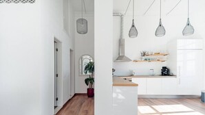 Eine moderne Küche mit weißen Schränken, einer Holzarbeitsplatte, hängenden Pendelleuchten und einem Blumentopf.