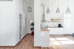 A modern kitchen with white cabinets, a wooden countertop, hanging pendant lights, and a potted plant. - Waterfront Living | Stunning Sea and Ocean Views (Setúbal)
