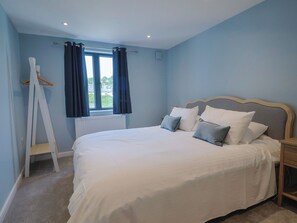 Ein Schlafzimmer mit einem Bett, einem Fenster mit Vorhängen, einem Heizkörper und einem Holzstuhl.