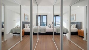 A modern bedroom with a large bed, bedside tables, and a city view through large windows. - Oceanique Penthouse in Leighton Beach (North Fremantle)