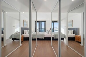 Ein modernes Schlafzimmer mit einem großen Bett, Nachttischen und Blick auf die Stadt durch große Fenster.