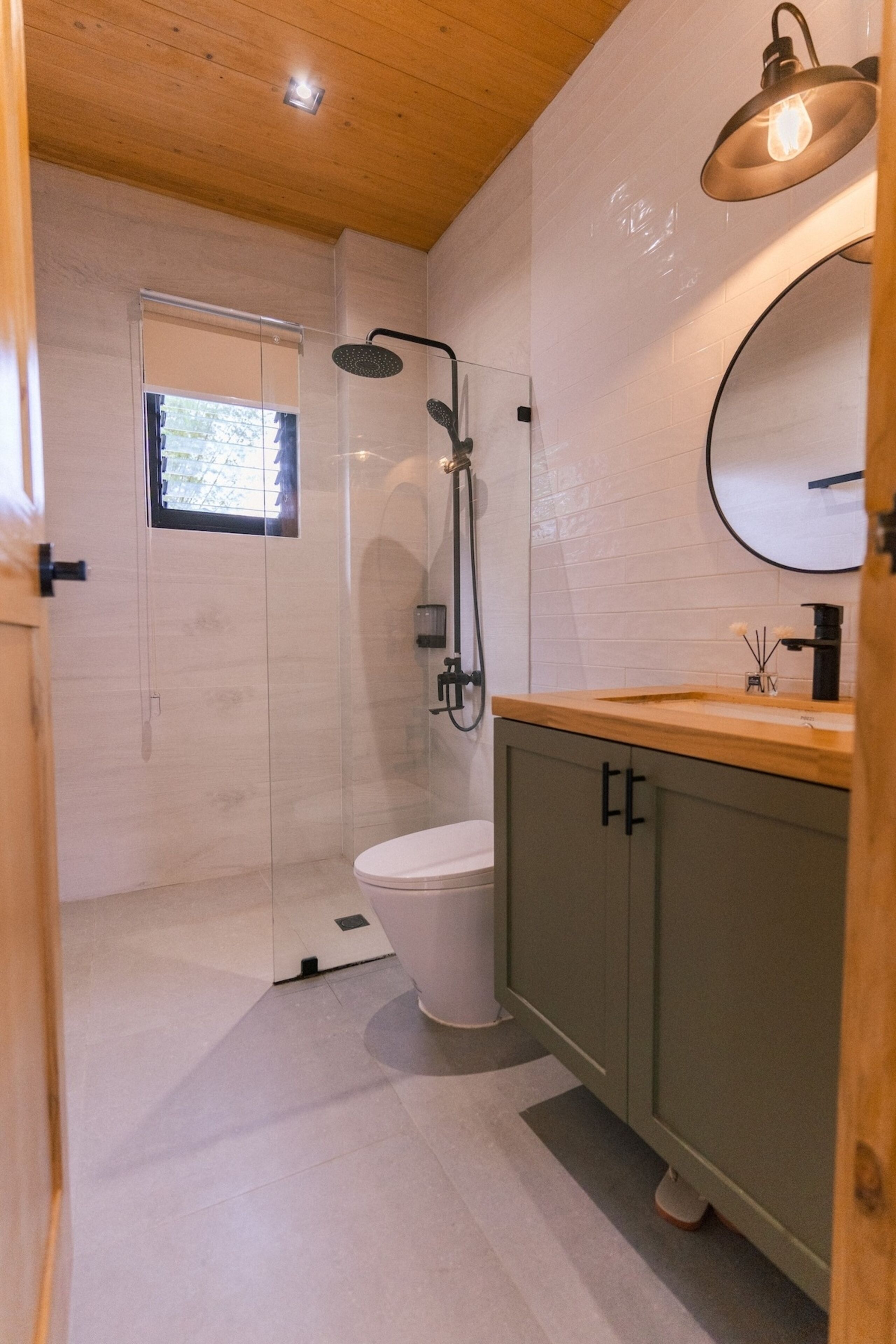 Un baño moderno con ducha de vidrio, inodoro, tocador de madera con lavabo y espejo.