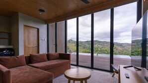 A modern room with a sofa, a small round table, and a large window offering a view of hills.