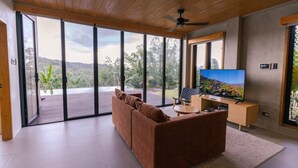 A modern living room with a large sliding glass door leading to a balcony, a brown sofa, a coffee table, and a flat-screen TV.