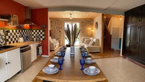 Ein Esszimmer mit langem Tisch, gedeckt für sechs Personen, einer Küchenzeile mit Herd und einer Treppe, die zu einer anderen Ebene führt.
