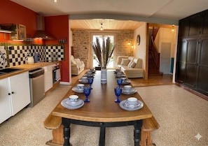 A dining room with a long table set for six, kitchen area with a stove, and a staircase leading to another level. - The Great Surtainville Shelter (Surtainville)