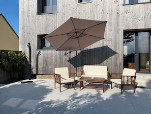 A patio with a wooden table and chairs, a large umbrella, and a wooden fence. - The Great Surtainville Shelter (Surtainville)