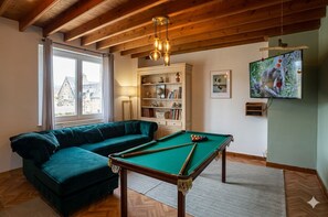 A cozy room with a pool table, a green sofa, a bookshelf, and a television. - The Great Surtainville Shelter (Surtainville)