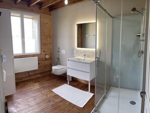 A bathroom with a wooden floor, a white sink, a toilet, and a glass shower enclosure. - The Great Surtainville Shelter (Surtainville)