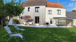 Ein modernes, zweistöckiges Haus mit überdachter Terrasse, Rasenfläche und Gartenmöbeln.
