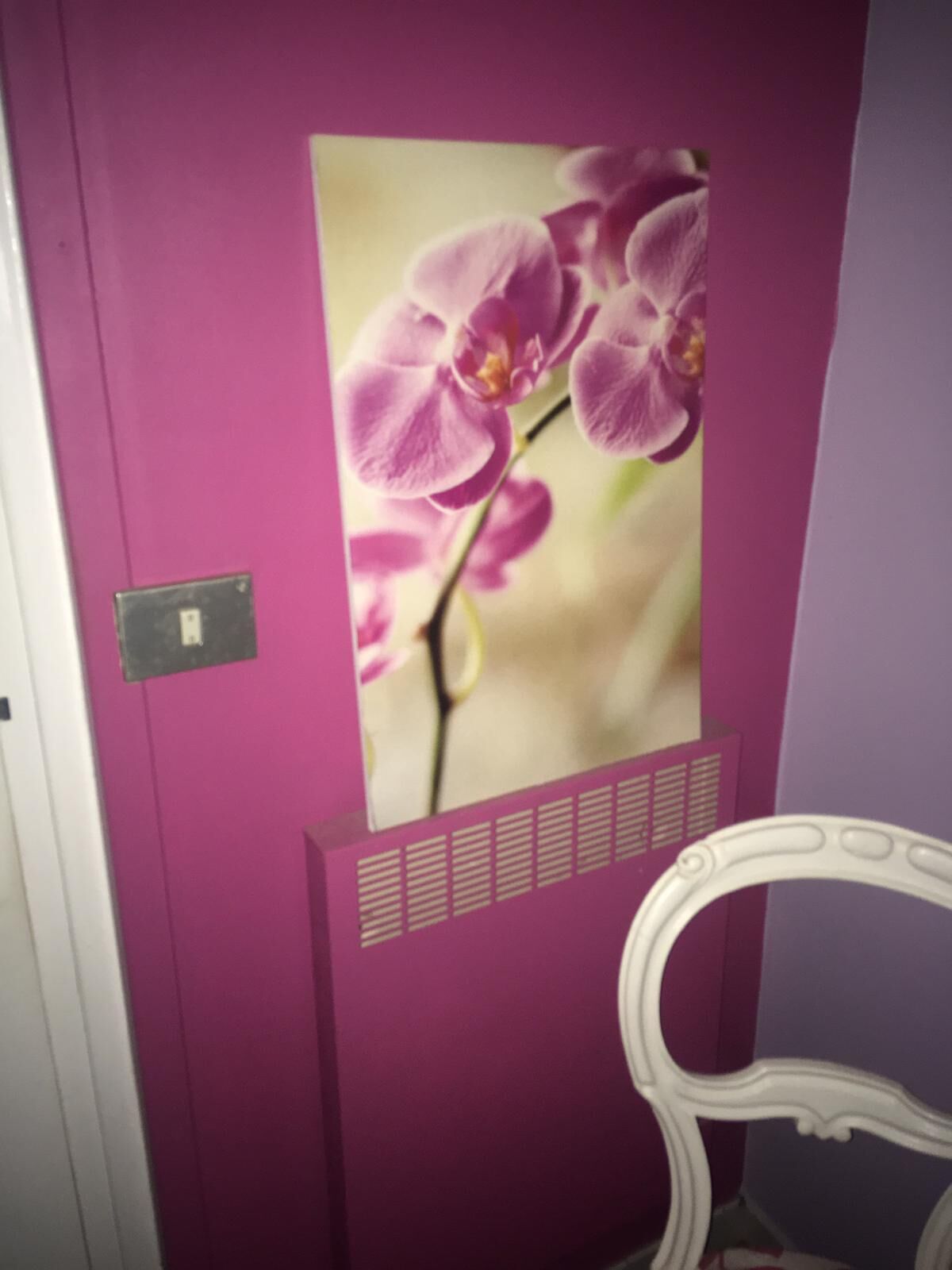 A room with a purple wall, a white chair, and a picture of pink orchids.