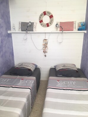 A room with two beds, a white wall, a shelf with decorative items, and a life ring. - View of port and sea (Le Barcarès)