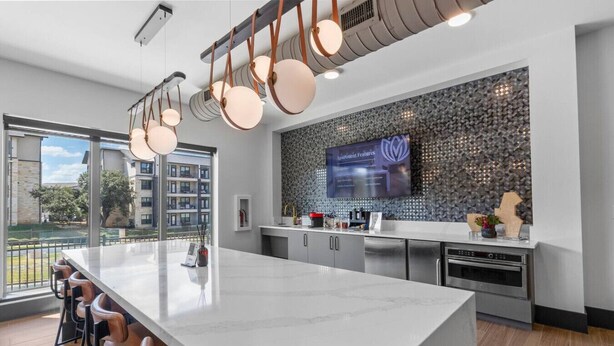 Una cocina moderna con una isla grande, taburetes de bar, electrodomésticos de acero inoxidable y un salpicadero decorativo.