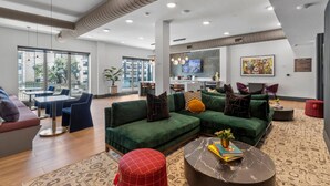 Una sala moderna con sofás verdes, un reposapiés rojo, una mesa de centro de mármol y una cocina al fondo.