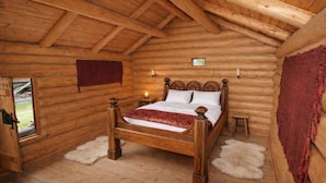 Une chambre dans un chalet en rondins, avec un lit en bois, une petite table de chevet, une fenêtre et une porte.