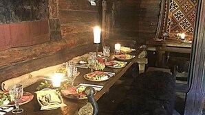 Une table à manger en bois, dressée avec des assiettes, des verres et des bougies, dans une pièce au décor rustique, où se trouve un chien noir.
