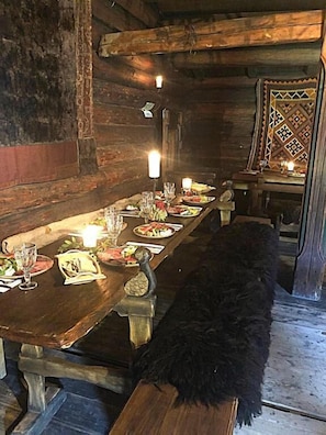 A wooden dining table set with plates, glasses, and candles in a rustic room with a black dog.