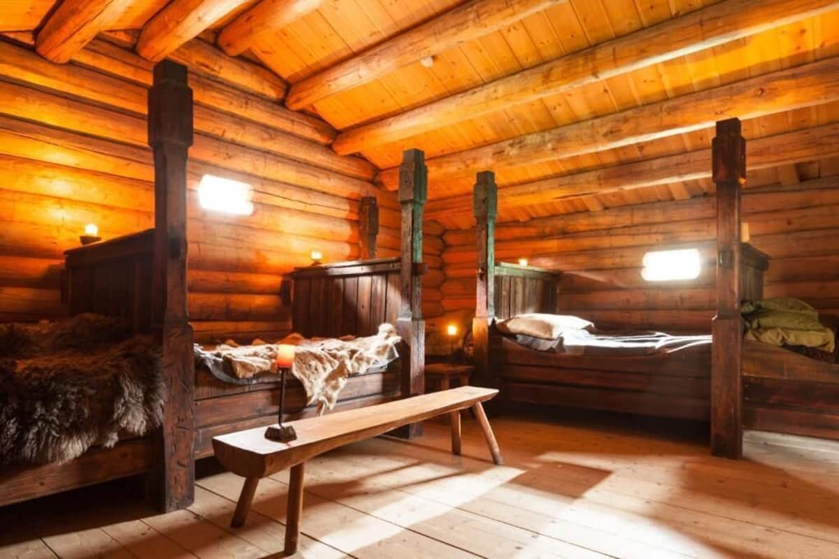 Ein Holzblockhaus-Interieur mit einer hölzernen Bank, zwei Betten und einem Kamin.
