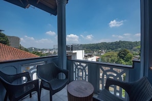 A balcony with wicker chairs and a round table, overlooking a cityscape with buildings and greenery. - Ceyloni Lake Residency - Kandy (Kandy)