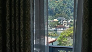 Blick durch ein Fenster mit Vorhängen auf einen See, Gebäude und einen bewaldeten Hügel.