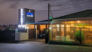 Ein Hotel mit einer Neonreklame, einem überdachten Parkbereich und einem umzäunten Garten.