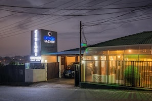 A hotel with a neon sign, a covered parking area, and a fenced garden. - Ceyloni Lake Residency - Kandy (Kandy)