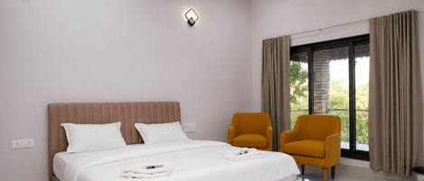 Una habitación de hotel moderna con una cama grande, dos sillones, un balcón con cortinas y dos luces fijadas a la pared.