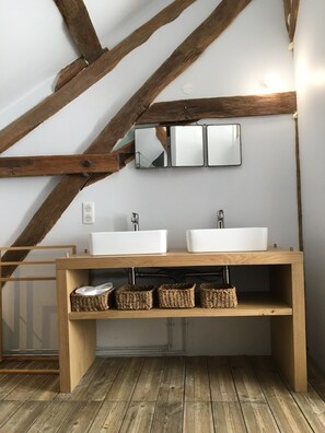 Un baño con vigas de madera, dos lavamanos, un espejo y cestas de mimbre.