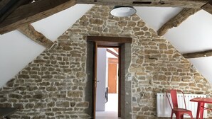 A stone-walled room with a sloped ceiling, a wooden beam structure, a table, and a chair. - 4-Star Longère “L'Albizia” with Morvan Views (Billy-Chevannes)