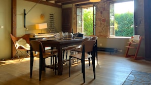 A dining area with a wooden table, chairs, pendant lights, a stone wall, and a window with a view of greenery. - 4-Star Longère “L'Albizia” with Morvan Views (Billy-Chevannes)