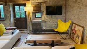 A rustic room with a stone wall, wooden beams, a fireplace, a television, a yellow chair, and a bed with pillows. - 4-Star Longère “L'Albizia” with Morvan Views (Billy-Chevannes)