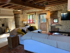 A rustic stone interior with a sofa, television, and a fireplace.