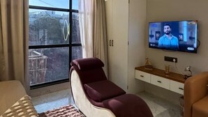 A modern hotel room with a large window, a massage chair, a TV, and a sofa. - Supreme Stays (Indore)