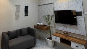 A modern living room with a grey sofa, a flat-screen TV, a marble-patterned floor, and recessed ceiling lighting. - Supreme Stays (Indore)
