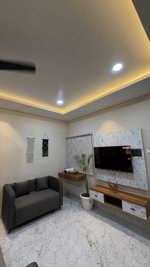 Un salon moderne avec un canapé gris, un téléviseur à écran plat, un sol à motifs de marbre et un éclairage encastré au plafond.
