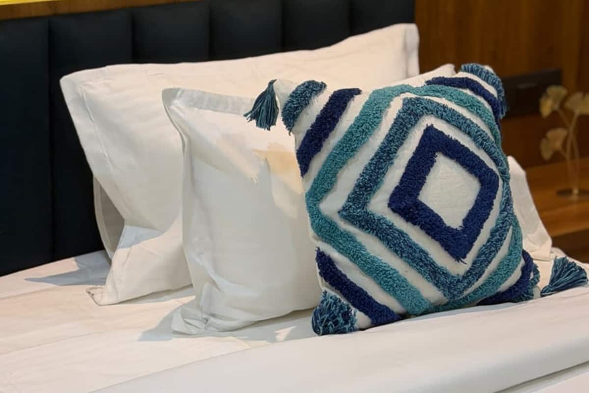 Una cama con ropa de cama blanca y una almohada estampada en azul y blanco.