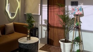 A modern living room with a sofa, a round coffee table, a potted plant, a small easel with a painting, and a wooden door. - Supreme Stays (Indore)