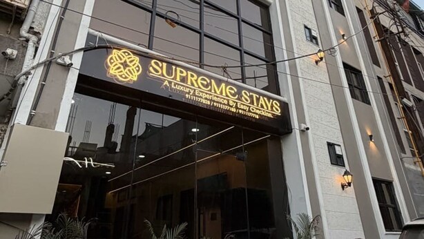 A building with a large glass entrance, a sign for 'Supreme Stays,' and potted plants in front. - Supreme Stays (Indore)