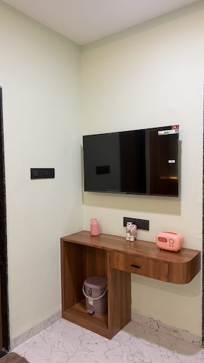 A room with a wooden desk, a television mounted on the wall, a pink kettle, and a small trash bin. - Supreme Stays (Indore)