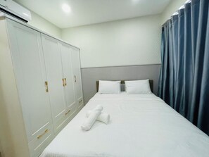 Ett hotellrum med en säng, vita gardiner, en garderob och en luftkonditioneringsanläggning.