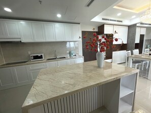 Una cocina moderna con armarios blancos, una encimera de mármol y un jarrón con flores rojas.