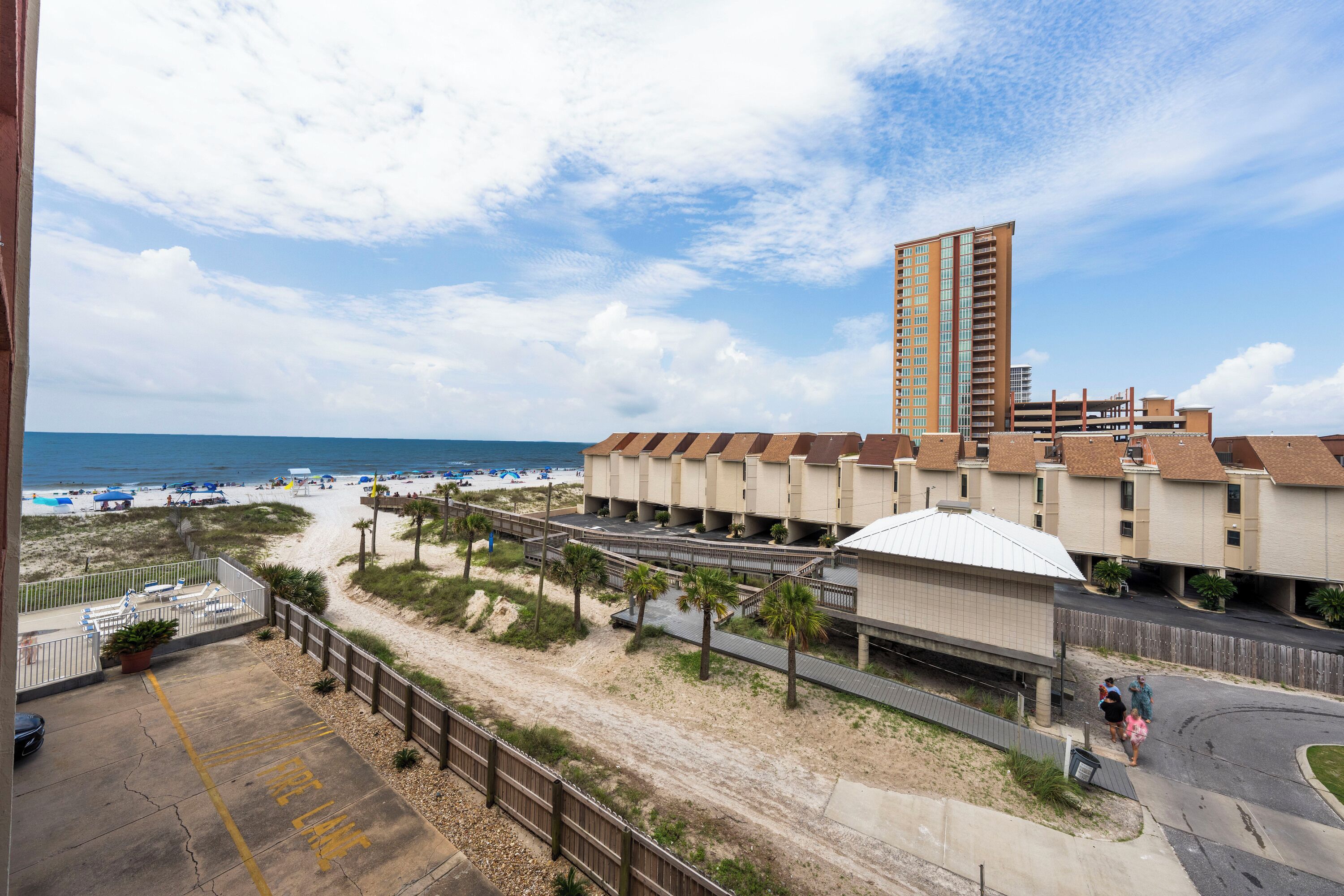 Een hotel aan het strand met een hoog gebouw, een zandstrand en een parkeerplaats.
