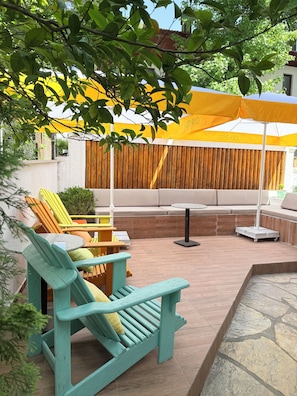 A patio with outdoor seating, including a teal lounge chair and a yellow umbrella providing shade. - Jasmine Suıts (ula)
